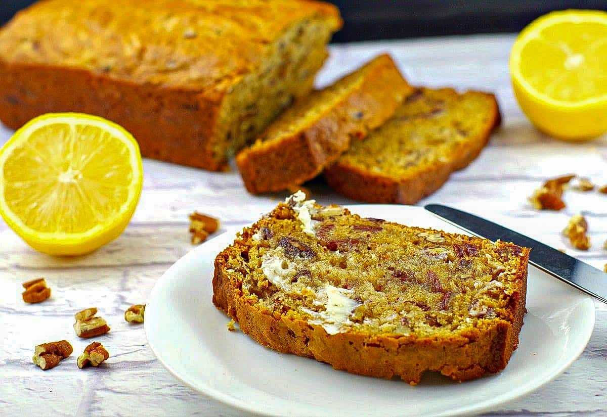 date nut loaf slice on white plate with remainder of loaf and 