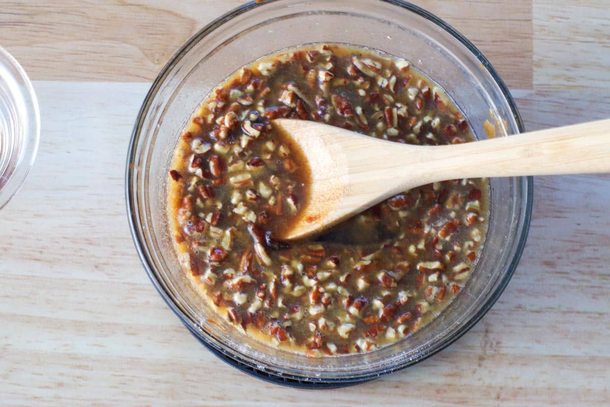 Pecans and vanilla extract added to mixture in glass bowl with wooden spoon