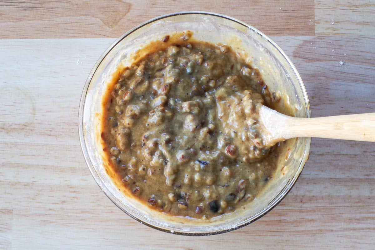 Dry ingredients added to wet ingredients in a glass bowl with wooden spoon