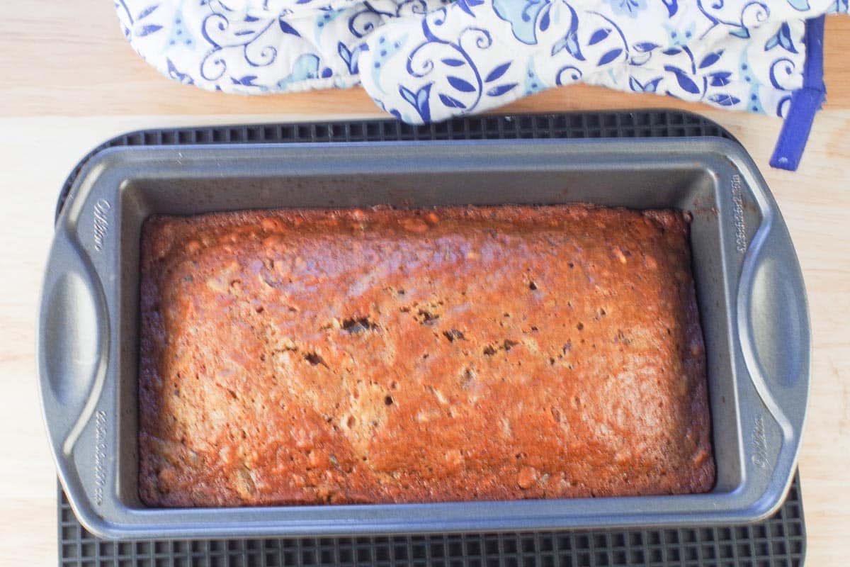 date nut loaf baked in a pan on trivet with oven mitts in background