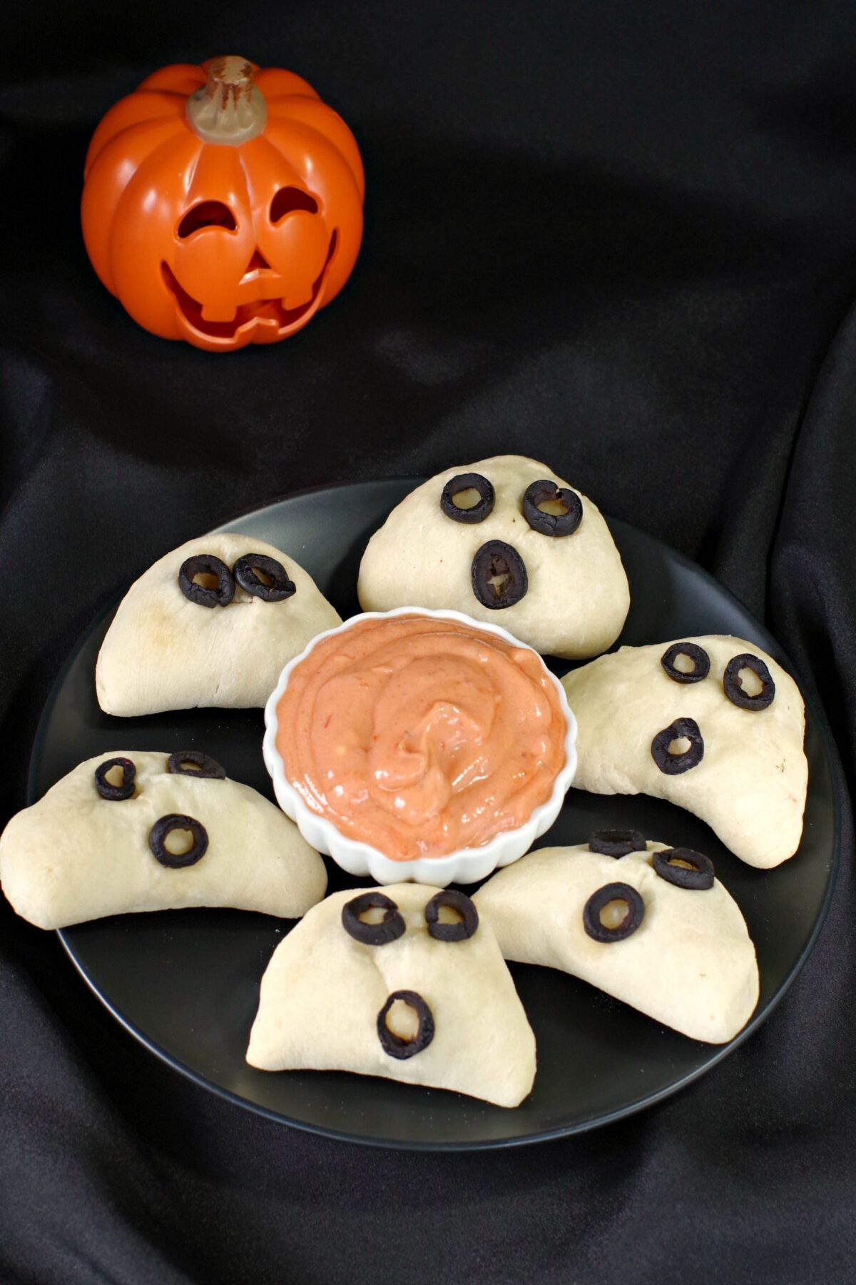 halloween pizza pockets on a black plate with dip in the middle and plastic jack o'latern in the background