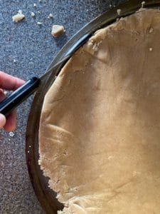 trimming gingerbread around edges of a pizza pan with knife