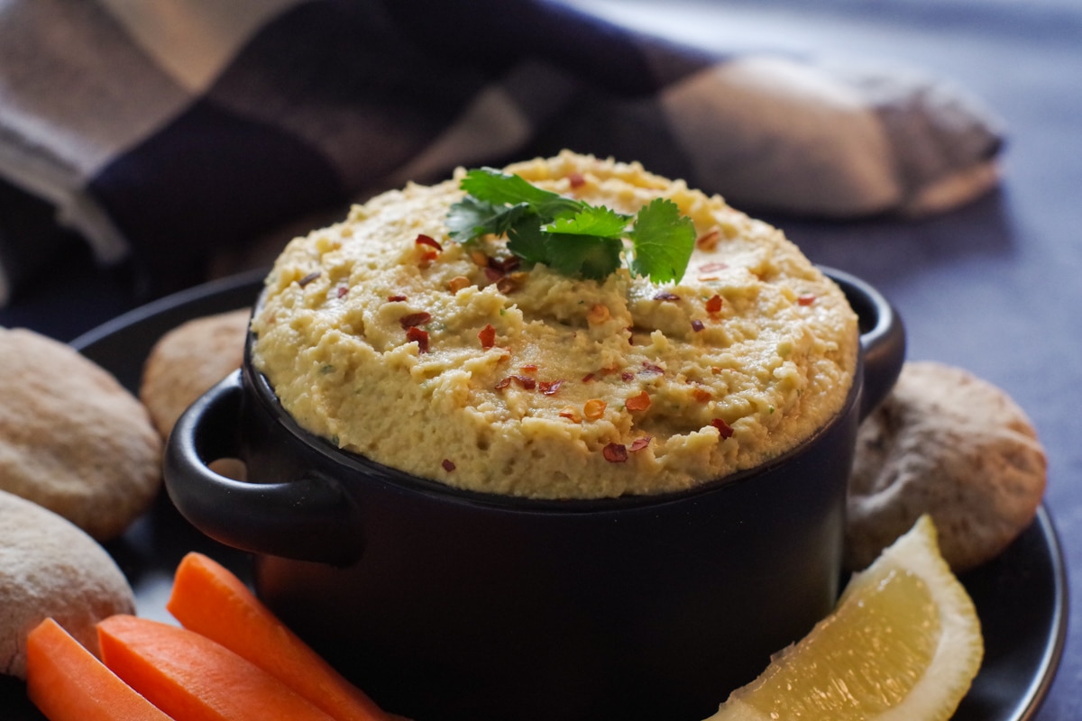 hummus in a black bowl on black plate with veggies and min pitas