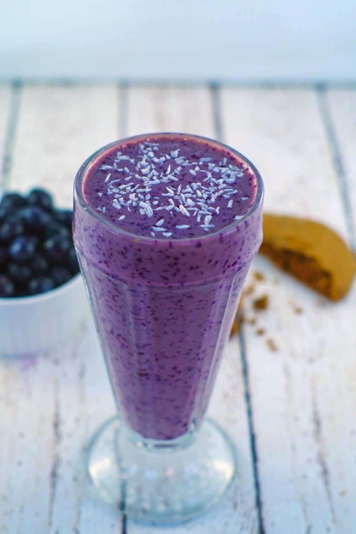 blueberry smoothie with almond milk on a white faux wooden surface with a half a cookie and blueberries in background