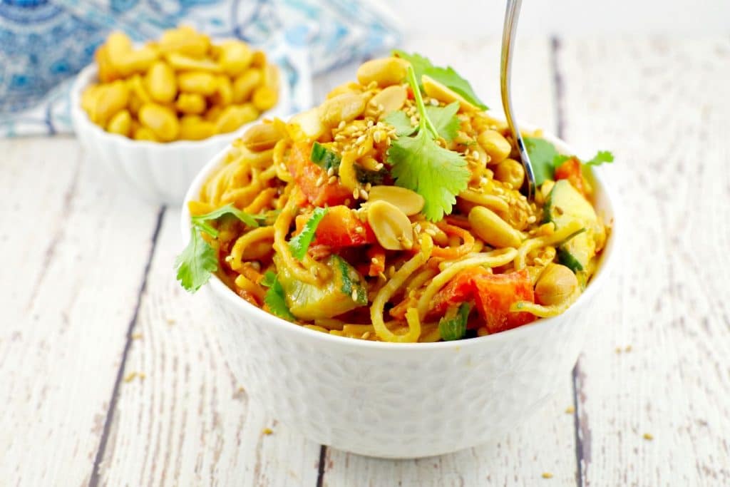 White bowl of noodles with peanuts, sesame seeds, cilantro and red peppers.