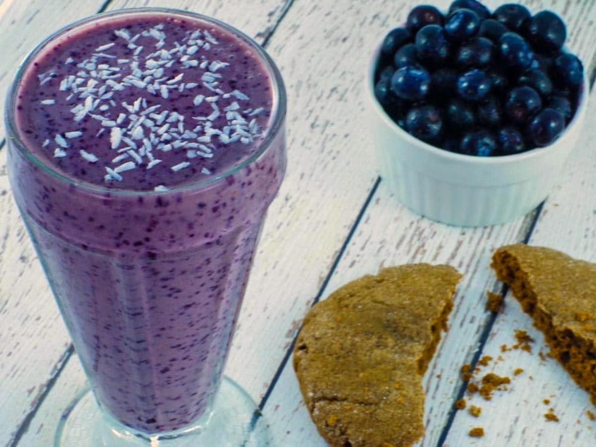 blueberry smoothie with almond milk on a white faux wooden surface with a half a cookie and blueberries in background