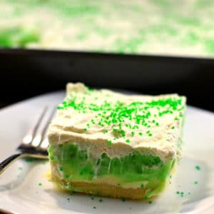 pistachio pudding dessert on a white plate with a fork, with a container of pistachio pudding dessert in the back