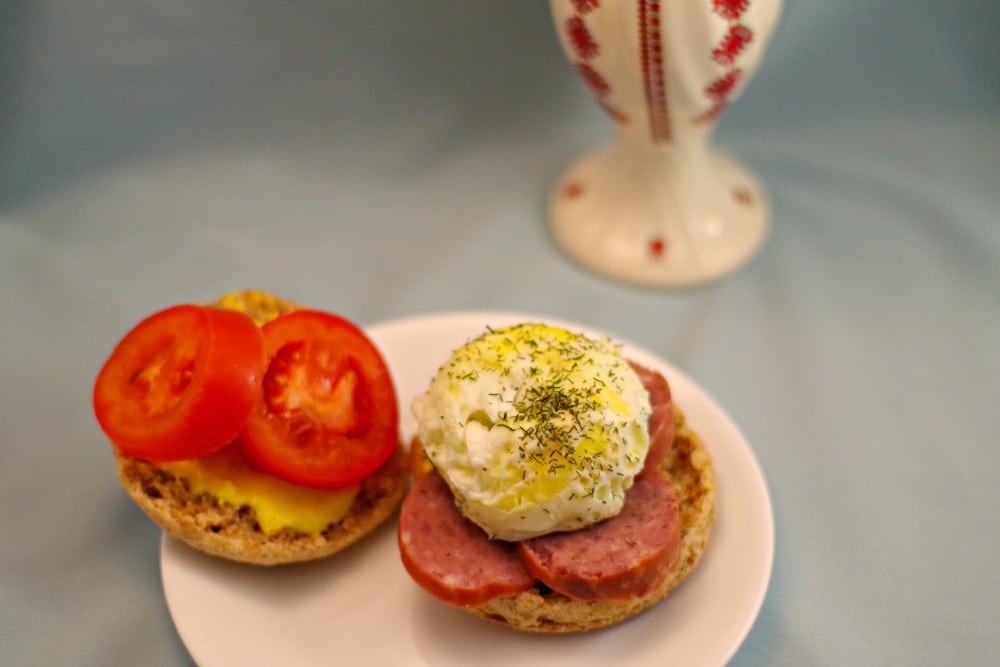 Ukrainian breakfast sandwich, open-faced, on a white plate with a Ukrainian patterned vase in the background