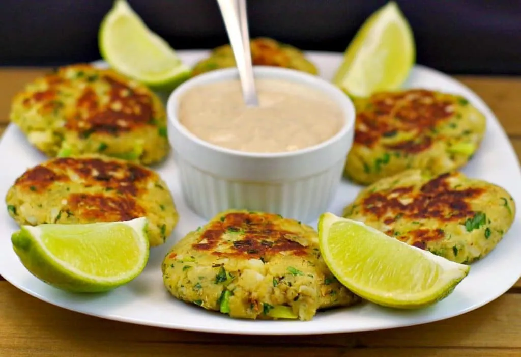 Pan-fried salmon patties on white plate, with dip in the middle and lime wedges