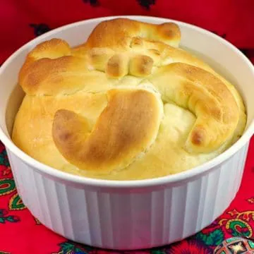 Paska bread in a round white casserole dish on red patterned surface
