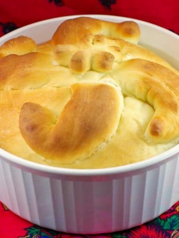 Paska bread in a round white casserole dish on red patterned surface