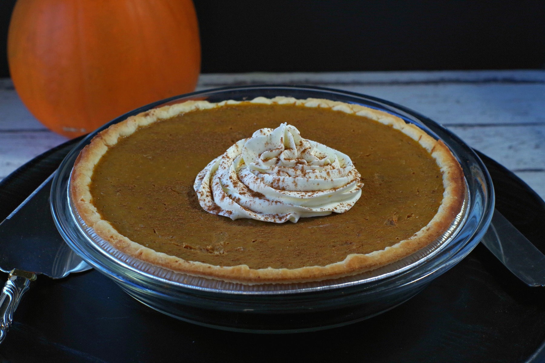 Whole pumpkin pie with pumpkin in the background, with whipped cream in the middle