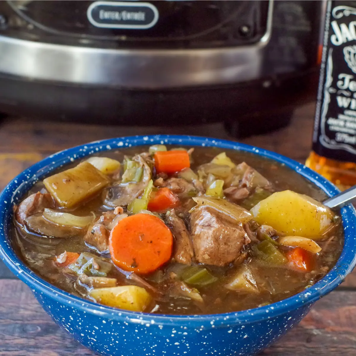 slow cooker beef stew in a blue bowl with slow cooker in the background