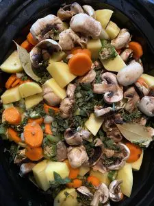 meat, veggies and herbs with liquid poured over, in slow cooker
