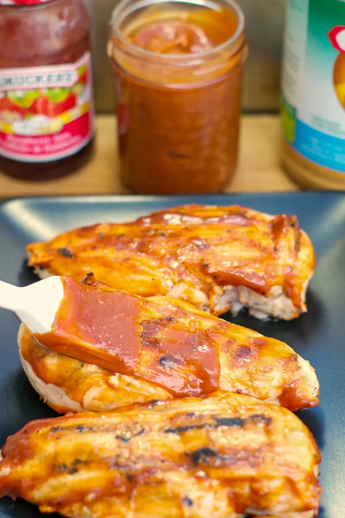 peanut butter BBQ sauce being spread on chicken on a black serving tray with jar of BBQ sauce in background