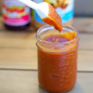BBQ sauce in a clear jar with brush being dipped in and peanut butter and jam in background