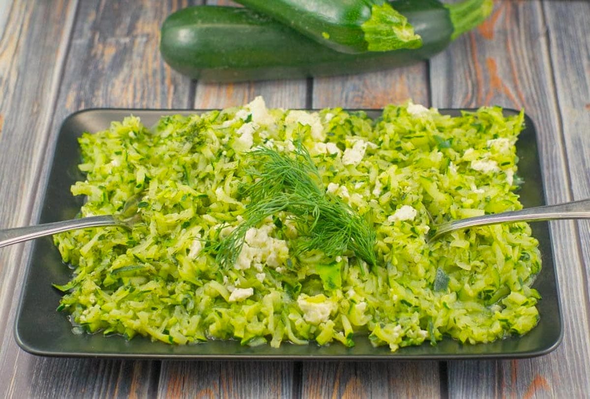 shredded zucchini on a black platter with zucchini in the background