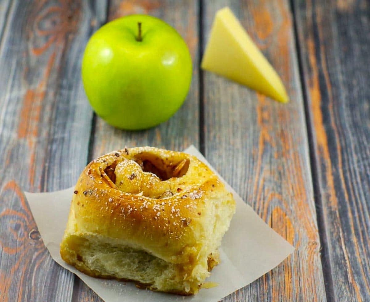 bread maker cinnamon rolls on a blue surface with a green apple and slice of gruyere cheese in background