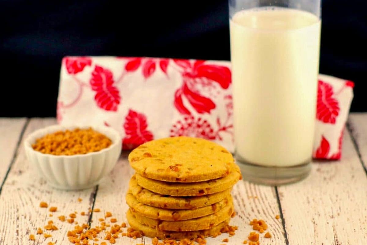 stack of butterscotch toffee cookies with a glass of milk and red and white tea towel in the background