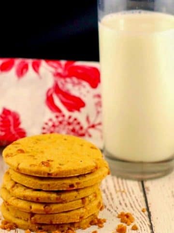 stack of butterscotch toffee cookies with a glass of milk and red and white tea towel in the background