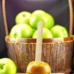 salted toffee halloween caramel apple on a white plate in front of a basket of green apples