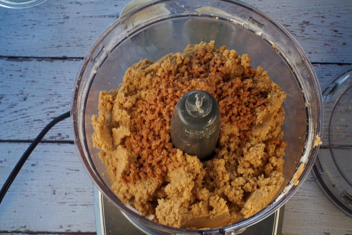 Toffee bits added to base ingredients in the bowl of a food processor.