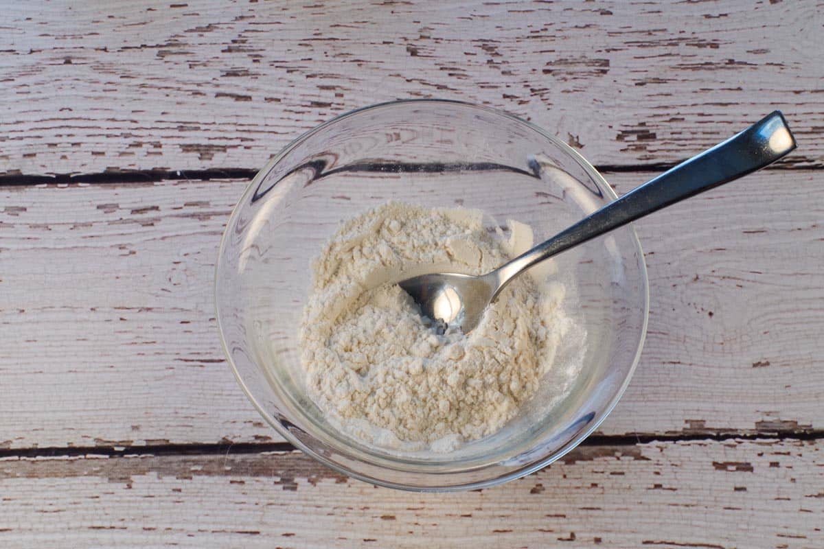 Flour and baking powder mixed together in a small glass bowl with a tablespoon in the bowl.