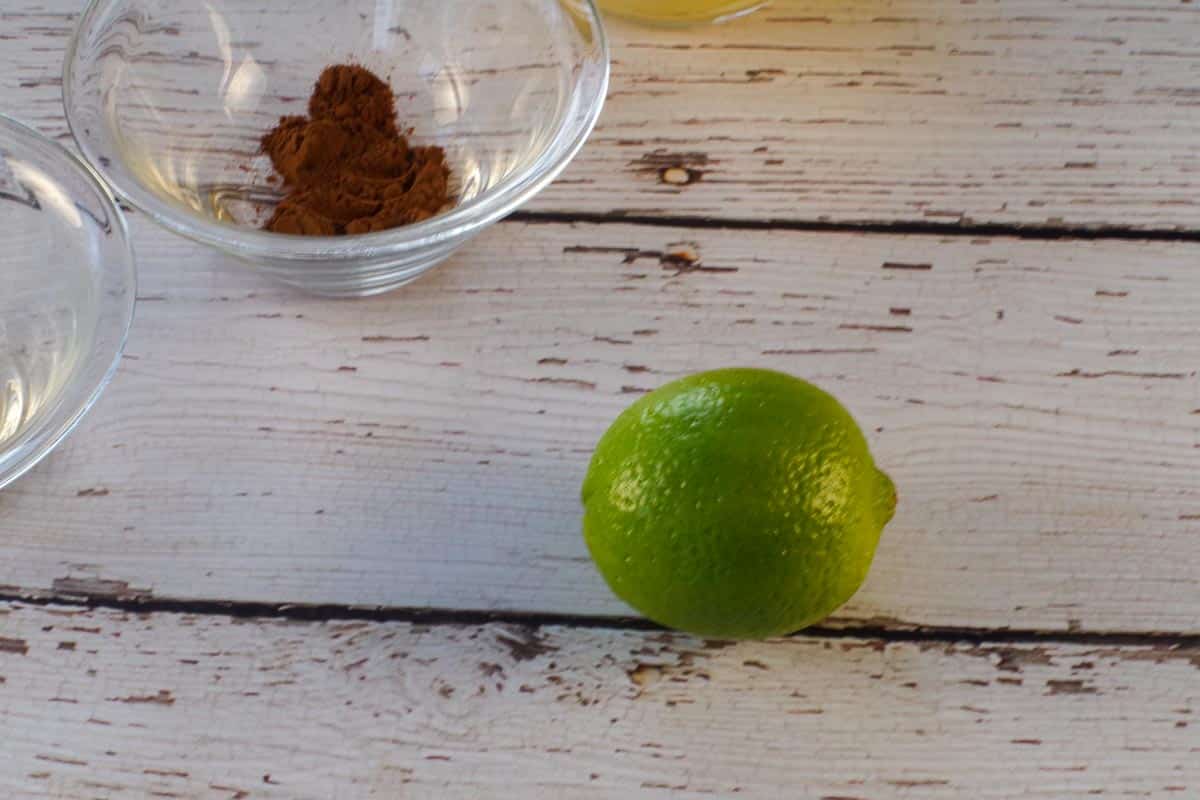 A lime on a faux wooden surface with a small glass bowl of cinnamon in the background.