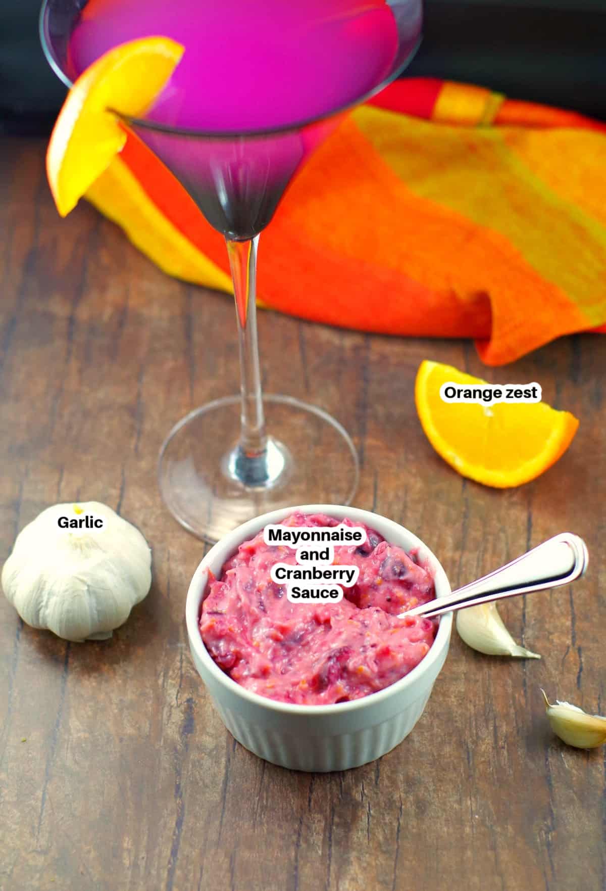 cranberry aioli ingredients on wooden surface with a tall Cosmopolitan drink in the background