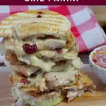 Pinterest pin with white text on cranberry colored background on top and bottom and photo of leftover turkey sandwich on a cutting board with checkered towel in background in the middle