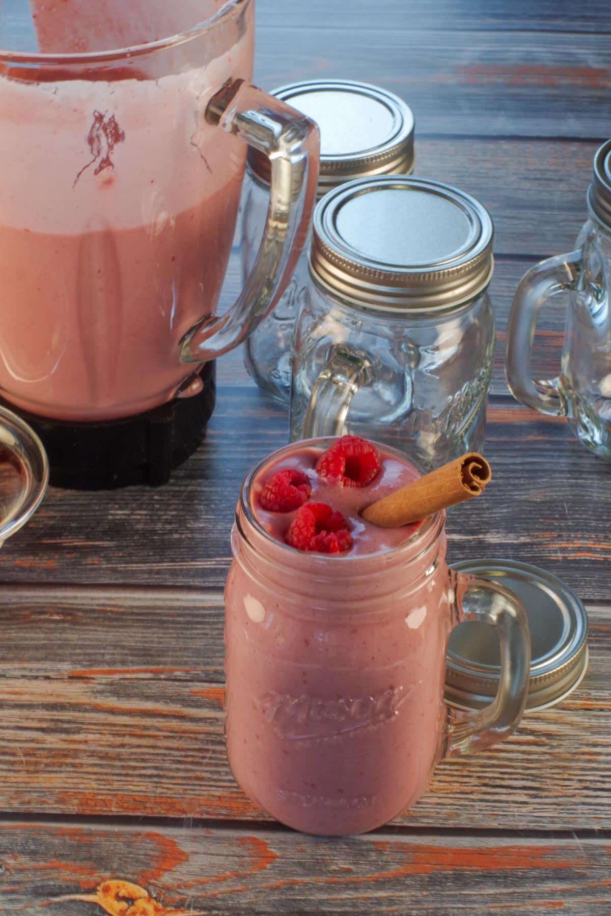 full glass of gingerbread smoothie garnished with raspberries and cinnamon stick with empty glasses and blender in the background