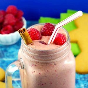 raspberry gingerbread smoothie with a bowl of raspberries and a gingerbread man in the background