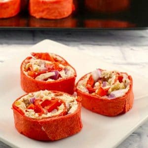 chicken tortilla pinwheels on a white plate with a tray of pinwheels in the background