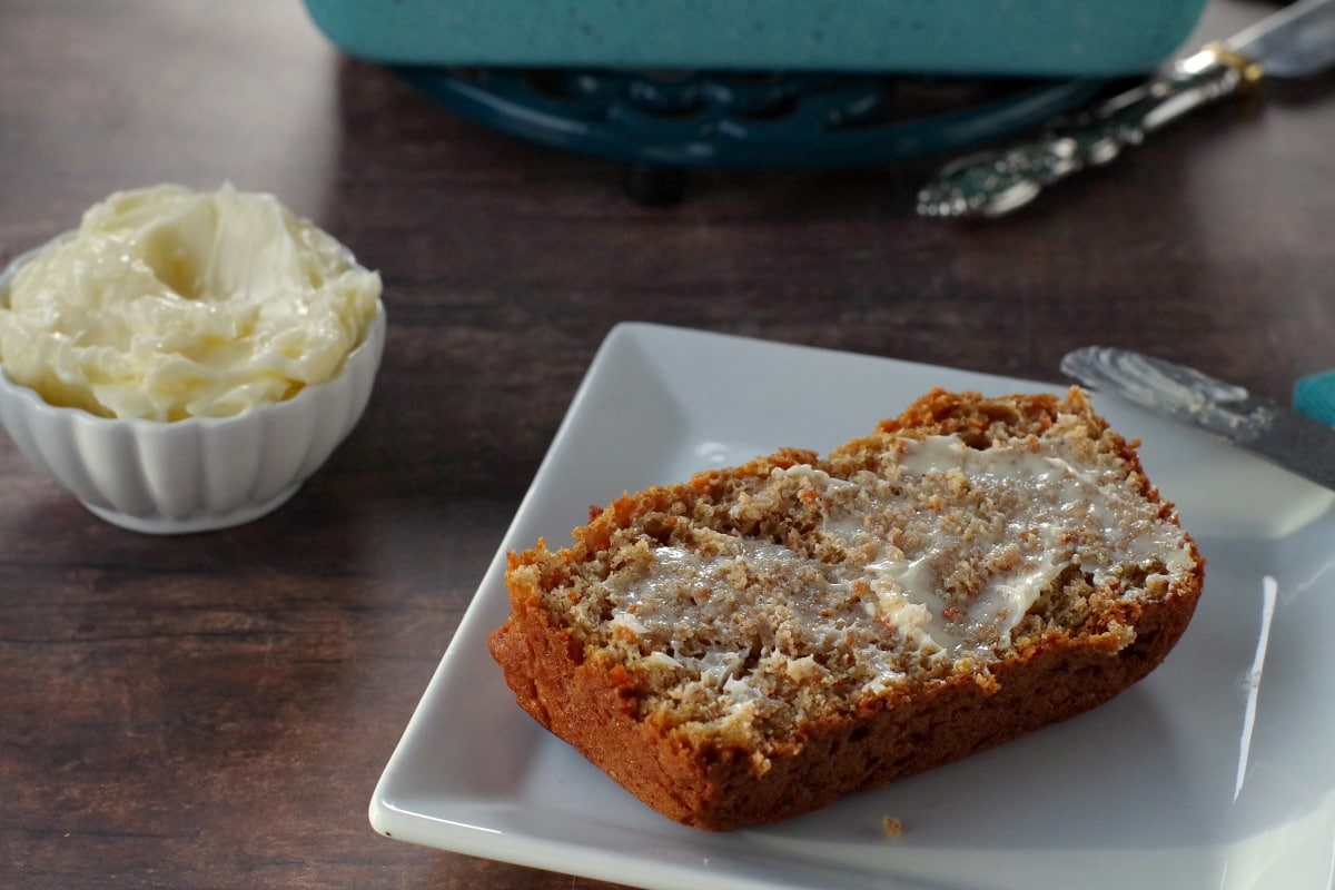 healthy carrot loaf slice with butter on a white plate with white dish of butter in the background