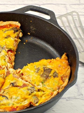 healthy breakfast pizza in cast iron pan with one piece missing and utensil (lifter) on the side