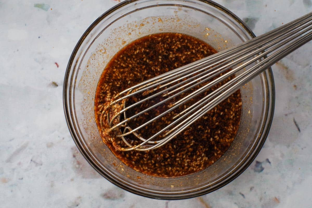 Peanut pasta salad dressing in a glass bowl with a whisk