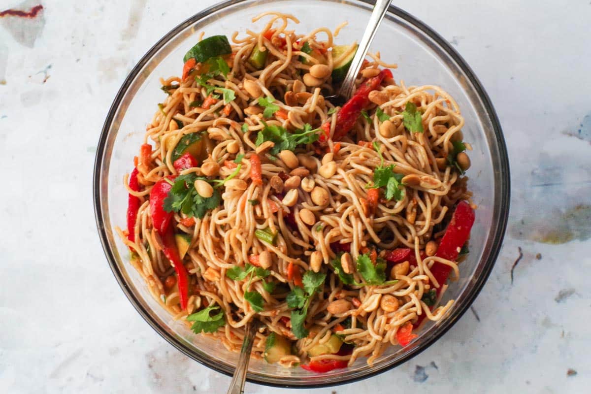 Dressing mixed into peanut pasta salad in a large glass bowl