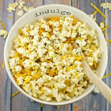 Savory popcorn in a white bowl, with the words 'indulge' on it, with a wood in it