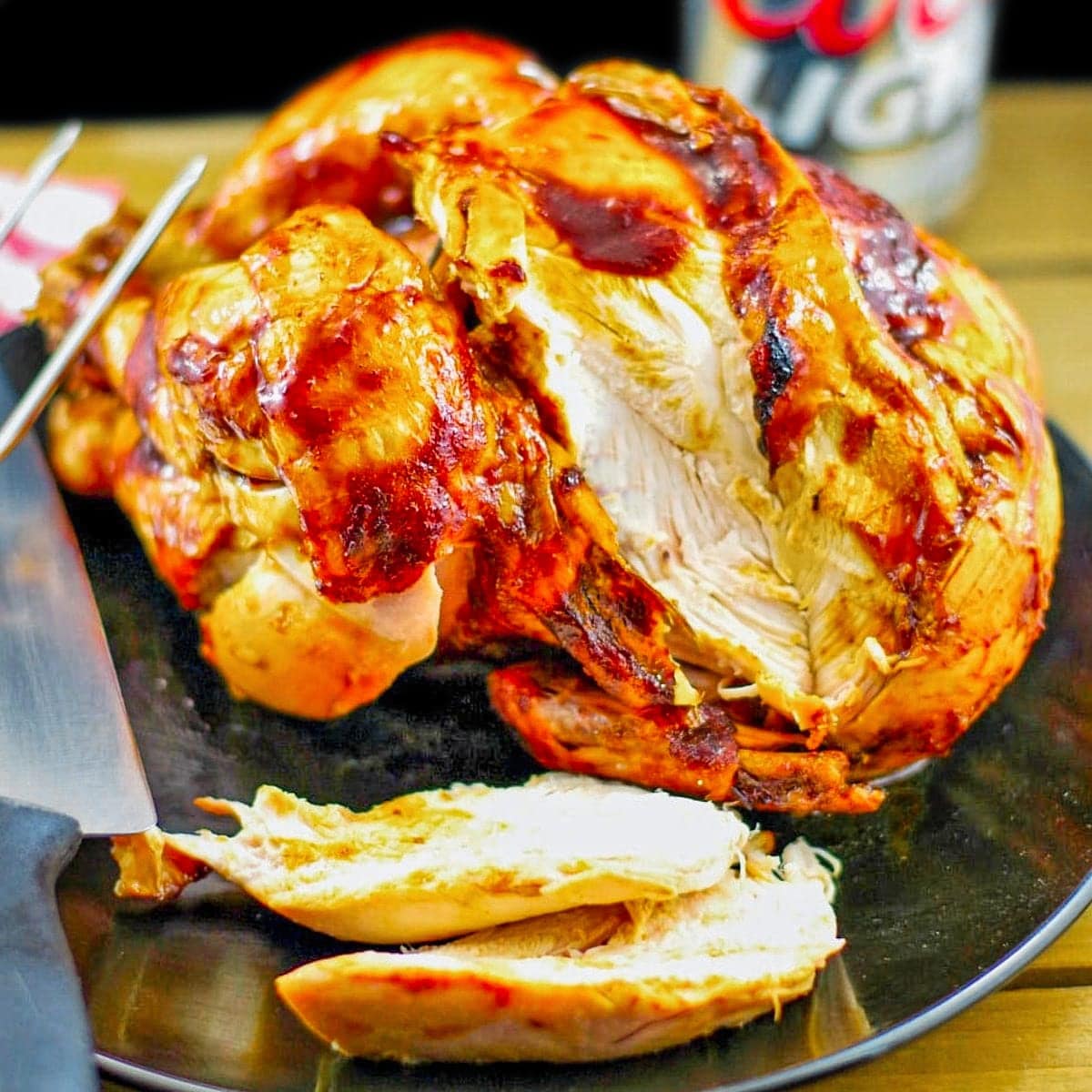 Beer butt chicken on a black plate with a couple of slices on plate and beer in background.