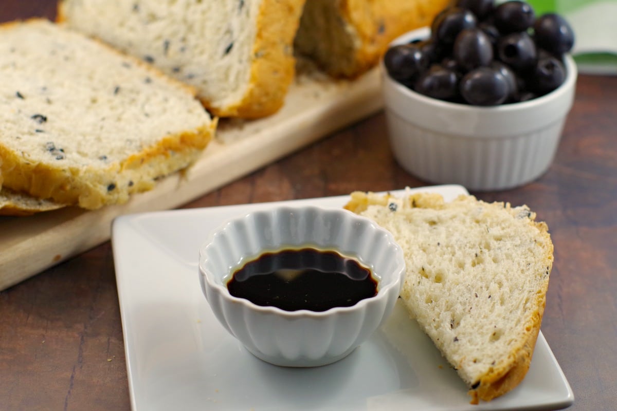 Loaf of Bread Machine Onion and Olive Bread, container of black olives and oil and vinegar in a dish with piece of bread for dipping