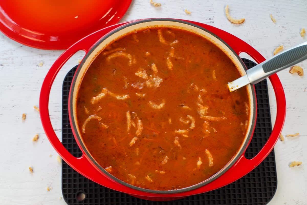 cooked carrot chowder in an orange Dutch oven with ladle, garnished with crisp onions