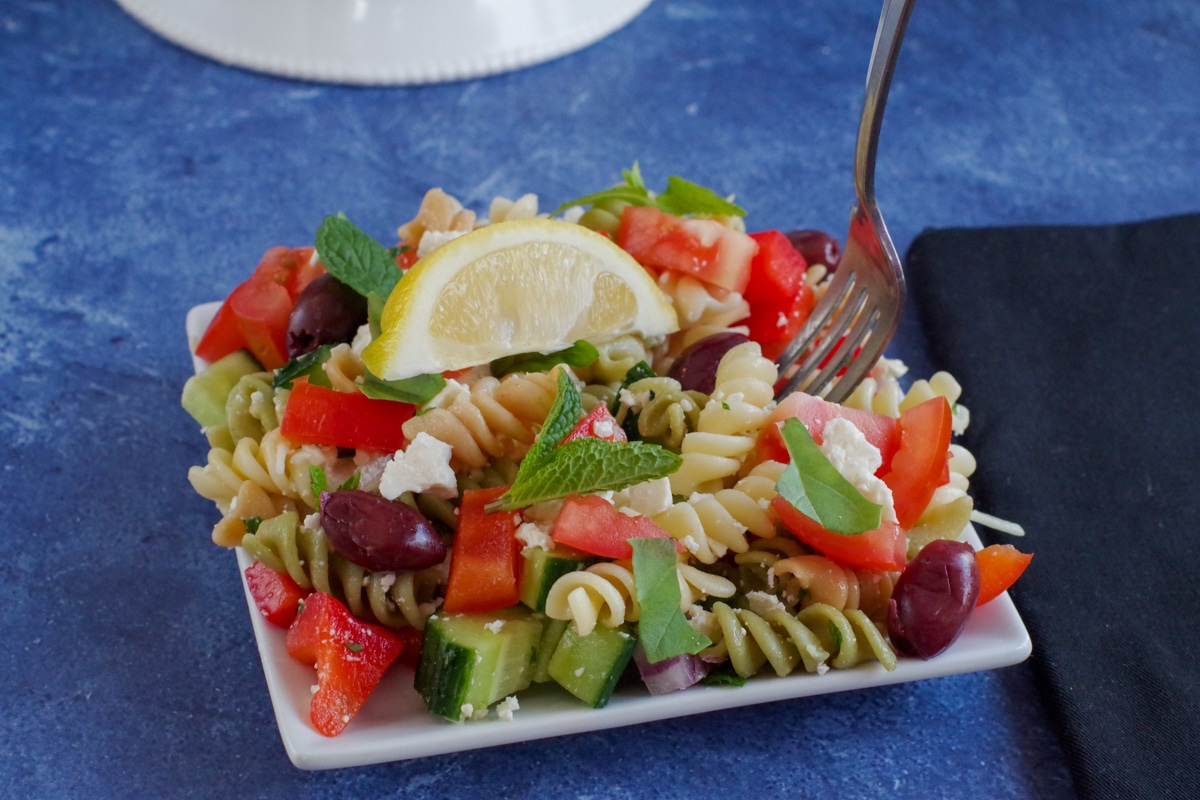 Greek pasta salad on white plate on blue surface