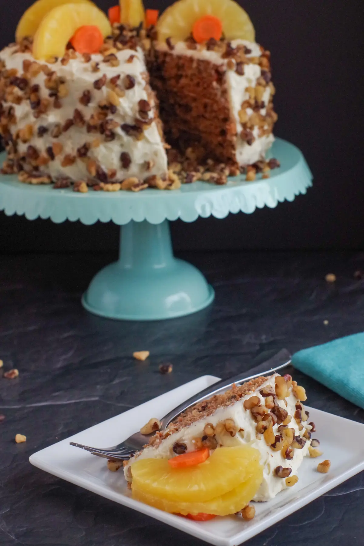 healthy and light carrot cake on a aqua cake stand in background with slice of cake on a white plate in front