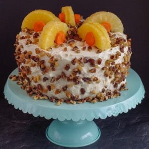 whole carrot cake decorated with pineapple and carrots on a aqua cake stand