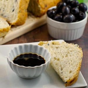 Loaf of Bread Machine Onion and Olive Bread, container of black olives and oil and vinegar in a dish with piece of bread for dipping