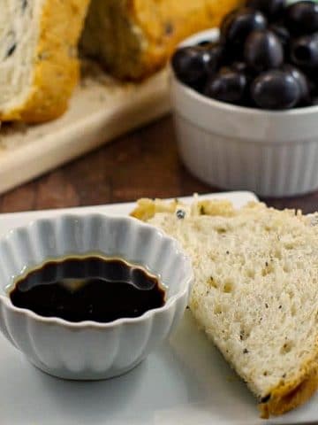 Loaf of Bread Machine Onion and Olive Bread, container of black olives and oil and vinegar in a dish with piece of bread for dipping