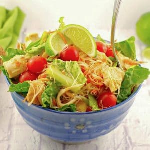 Thai Chicken Noodle Salad in a blue bowl on white surface with green napkin in background
