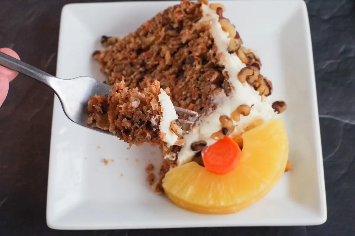 slice of healthy and light carrot cake on a plate with fork lifting bite out of it