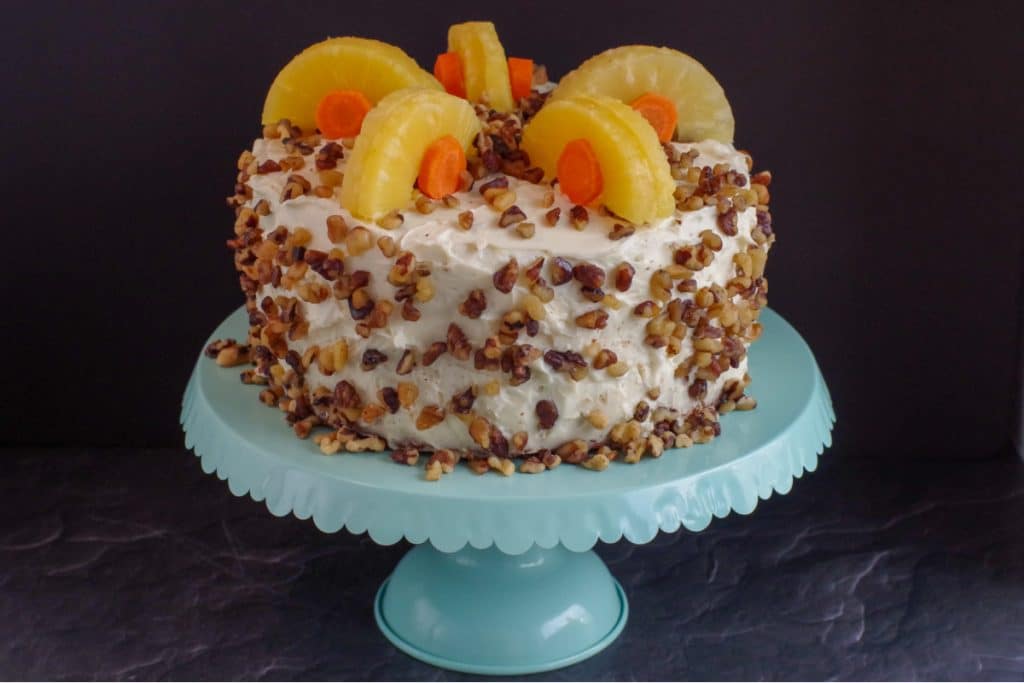 whole carrot cake decorated with pineapple and carrots on a aqua cake stand