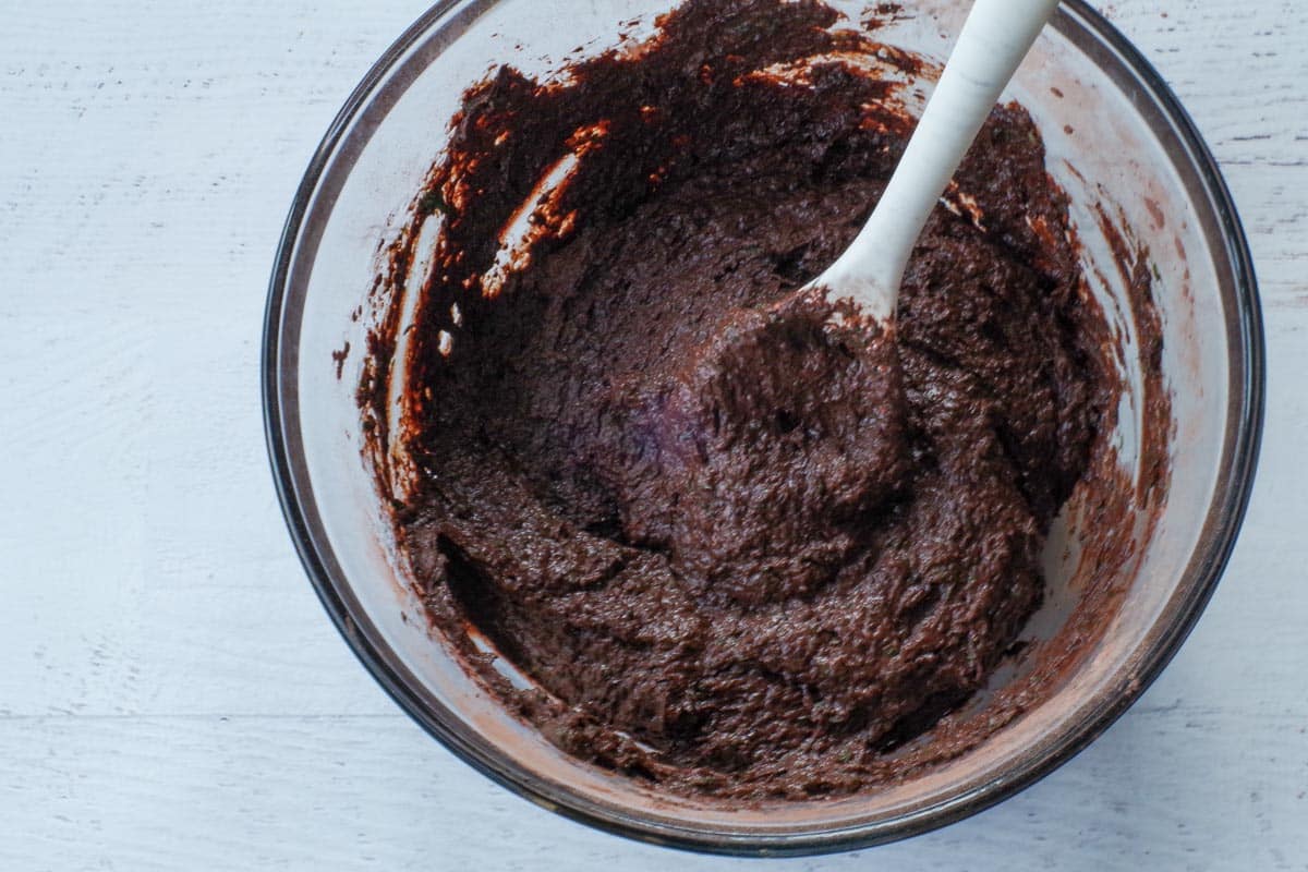 melted chocolate mixed into batter in a large glass bowl with marbled silicone spoon